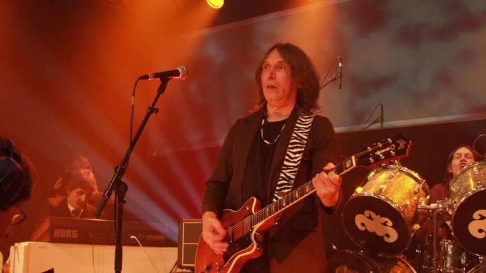 Mann mit langen Haaren und Gitarre auf der Bühne.