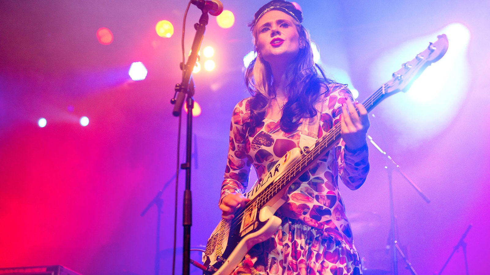 Kate Nash hat einen Bass vor sich hängen und sieht weiter über der Kamera hinweg.