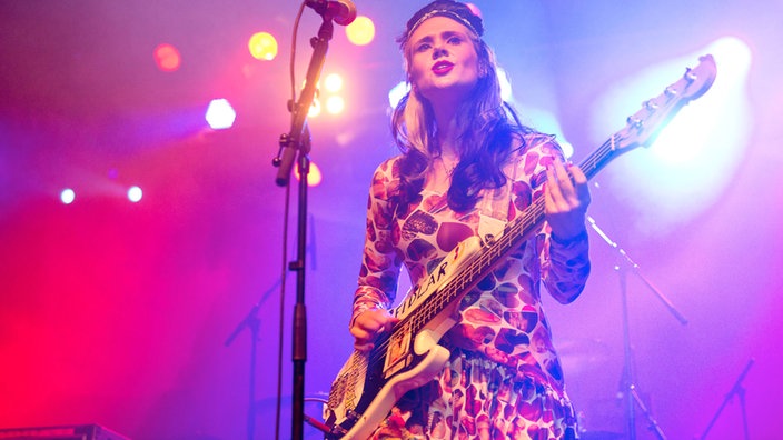 Kate Nash hat einen Bass vor sich hängen und sieht weiter über der Kamera hinweg.