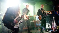 Drei Musiker von Grande Roses auf der Bühne - sie alle tragen schwarze Lederjacken.