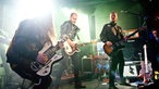 Drei Musiker von Grande Roses auf der Bühne - sie alle tragen schwarze Lederjacken.