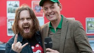 Der langhaarige und bärtige Frontmann der Band Monster Truck steht mit dem Moderator des Rockpalastes auf der Straße.