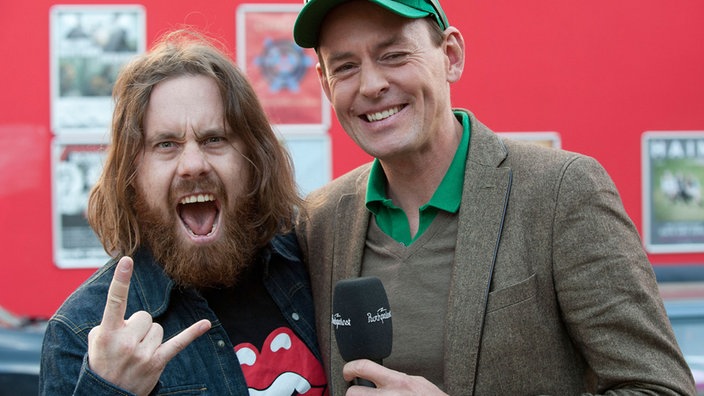 Der langhaarige und bärtige Frontmann der Band Monster Truck steht mit dem Moderator des Rockpalastes auf der Straße.