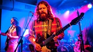 Der Frontmann der Band zieht seine Gitarre zu sich heran und spielt mit offenem Mund und geschlossenen Augen.