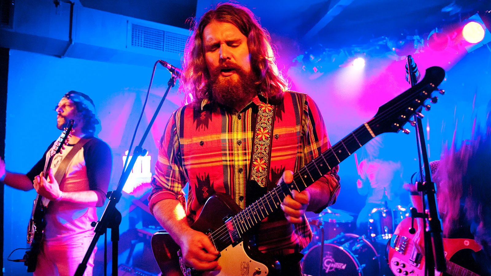 Der Frontmann der Band zieht seine Gitarre zu sich heran und spielt mit offenem Mund und geschlossenen Augen.