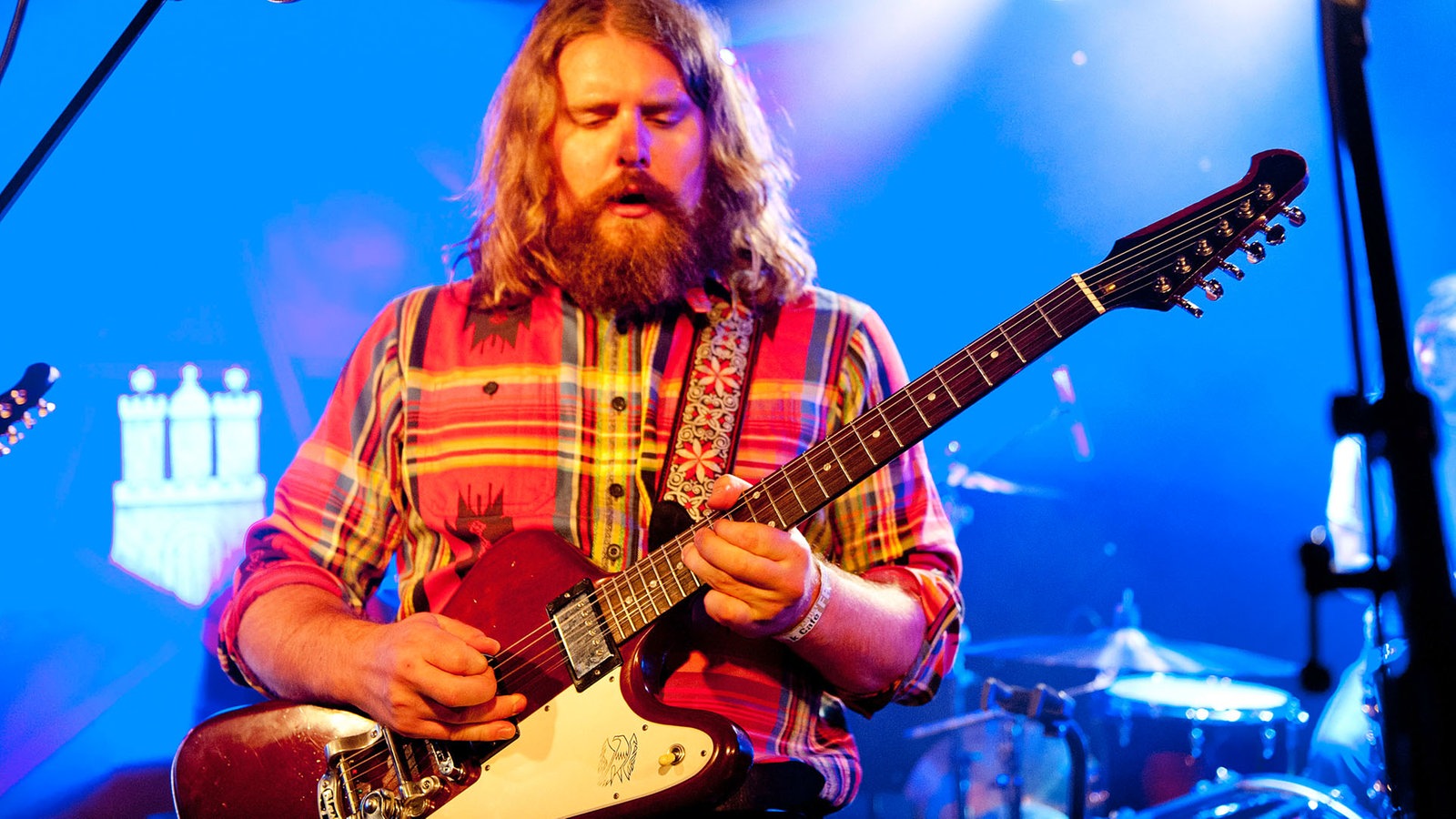 Der rundliche Frontmann der Band sieht angestrengt nach unten und spielt auf seiner Gitarre.