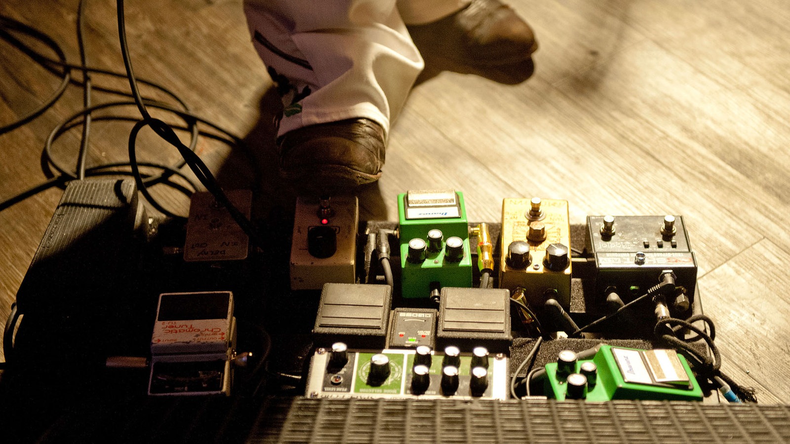 Man sieht den Fuß einer der Gitarristen, der gerade eines seiner Effektgeräte für die Gitarre am bedienen ist.