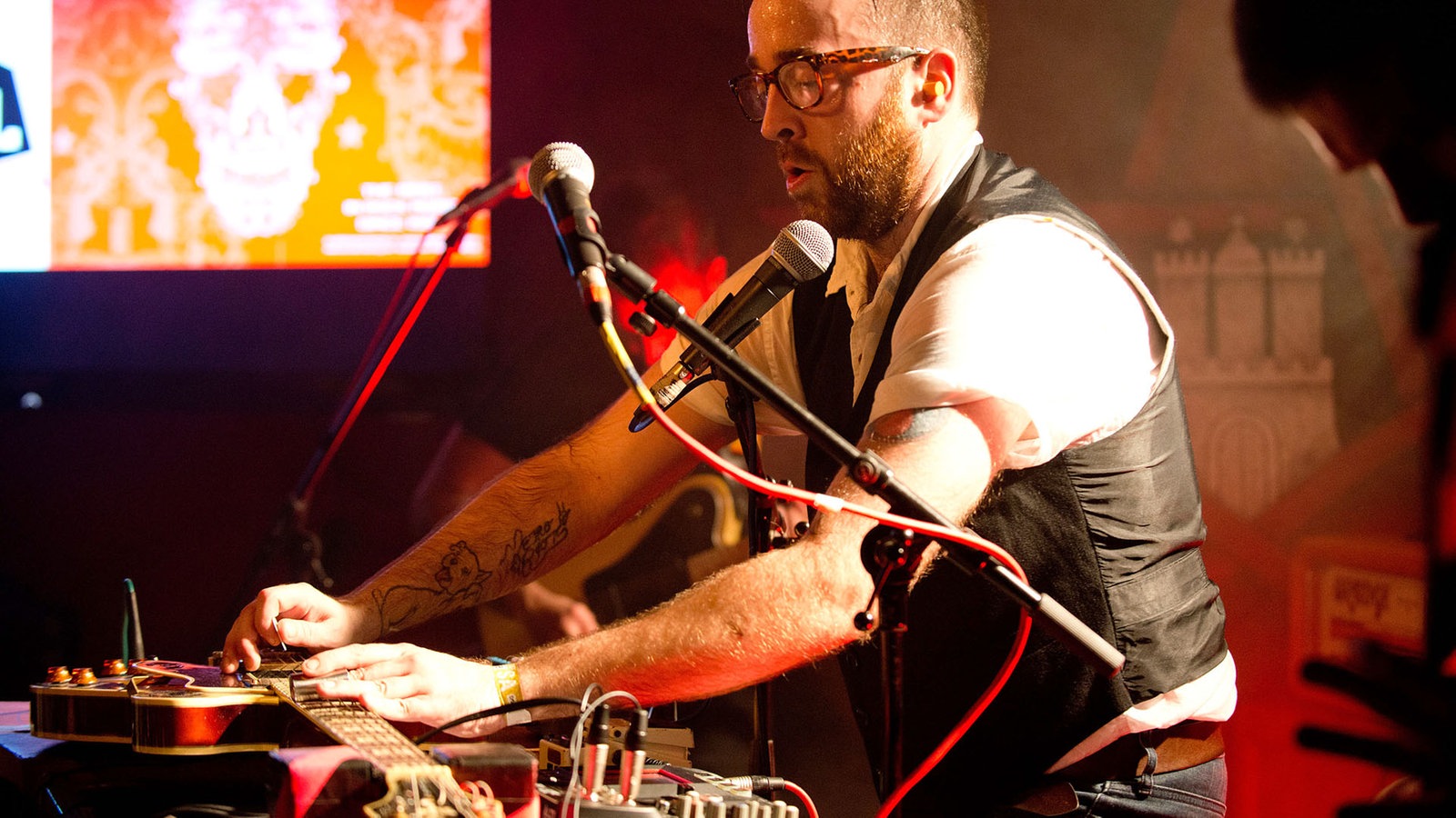 Antlered Man Musiker zupft eine vor ihm auf einem Tisch liegende Gitarre.