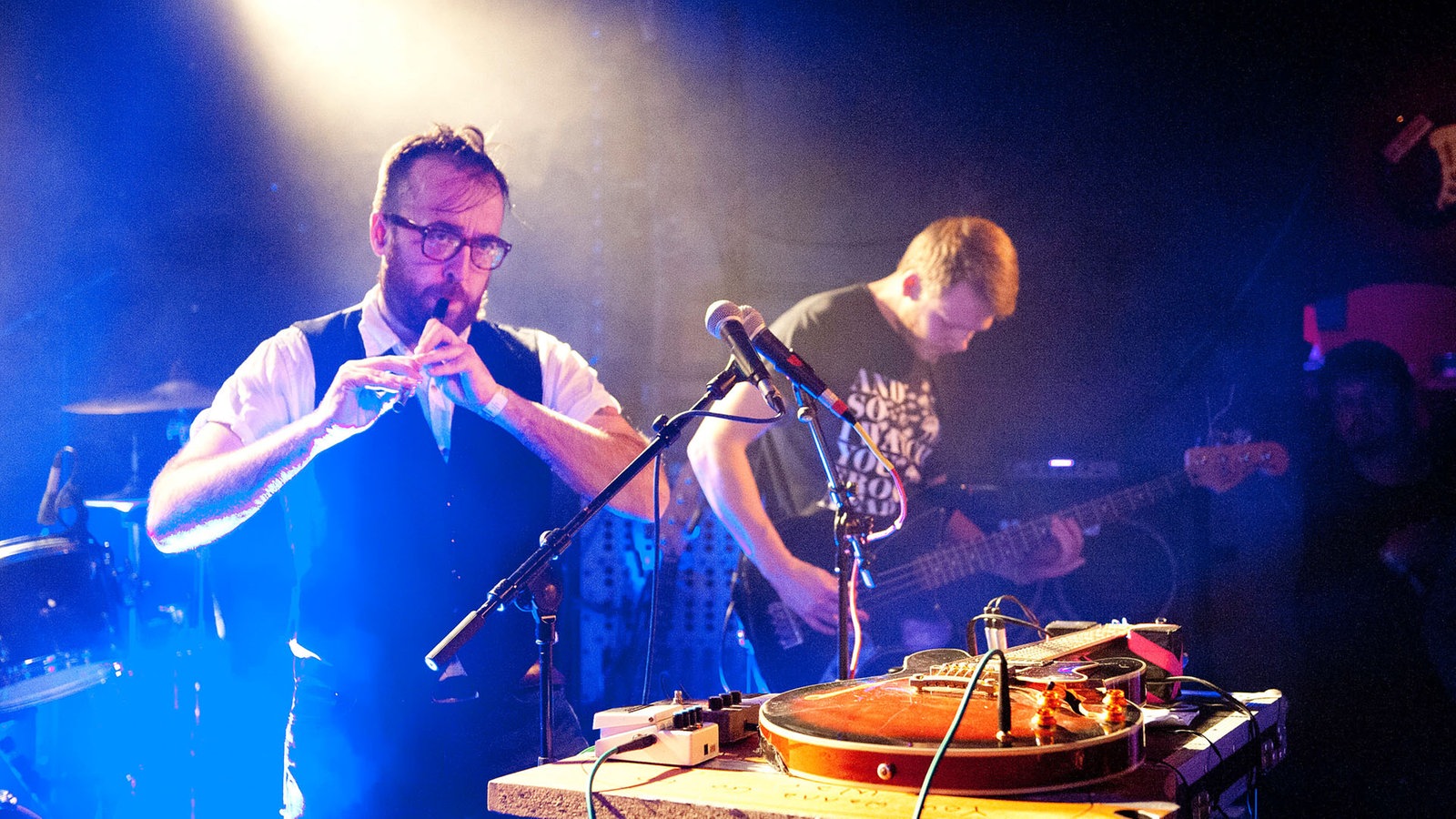 Zwei Musiker von Antlered Man, der eine spielt eine kleine Flöte, der andere Bass. Vor ihnen ein Tisch mit diversen Effektgeräten.