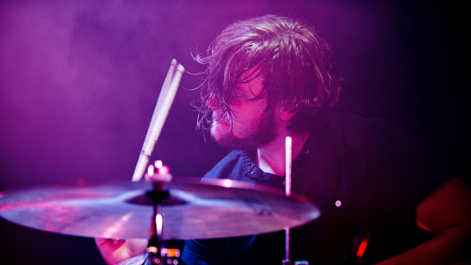 Ein seitlicher Blick auf den Drummer, dem beim Spielen die Haare ins Gesicht fallen. Er wirkt versunken.