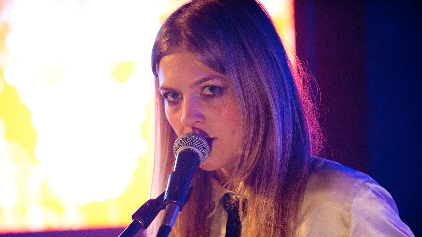 Kill It Kid Sängerin Stephanie Ward. Sie singt, den Mund dicht am Mikro, und schenkt der Kamera einen intensiven Blick.