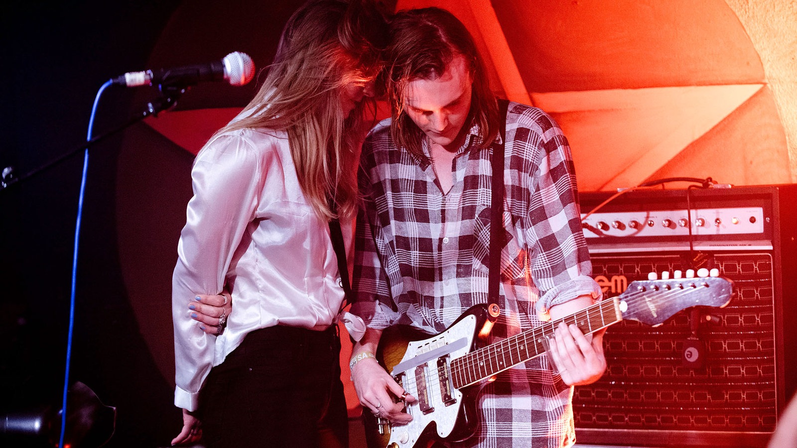 Die Sängerin steht ganz nah bei ihrem Bandkollegen, der Gitarre spielt. Die beiden stecken regelrecht die Köpfe zusammen.