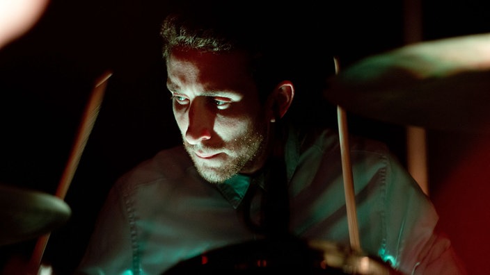 Ausdrucksstarke Nahaufnahme des Drummers, der einen gespannten, konzentrierten Gesichtsausdruck hat.