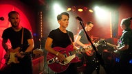 Vier Musiker der Band New Desert Blues. Im Mittelpunkt der adrett frisierte Sänger mit einer besonders auffälligen Gitarre. Er schaut ein wenig bedröppelt.