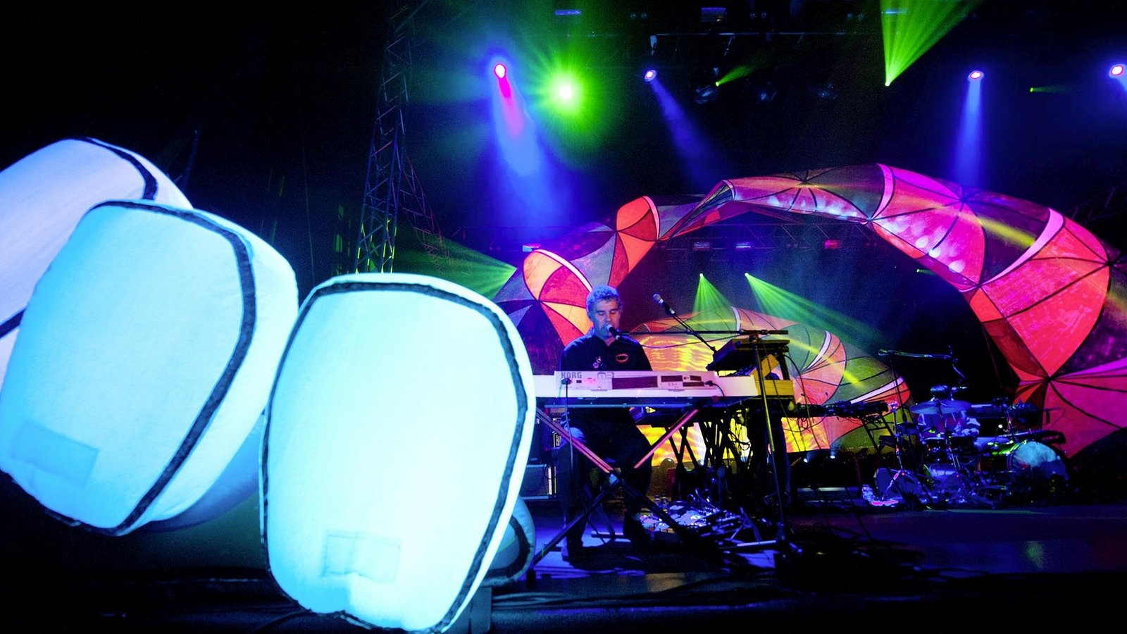 Leuchtende weiße Luftpolster vor der Bühne und leutende bunte Lichtbögen auf der Bühne, dazwischen ein Mitglied der Band Animal Collective.