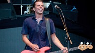 Bassist der Band Sportfreunde Stiller lächelt sichtlich zufrieden und durchgeschwitzt Richtung Publikum