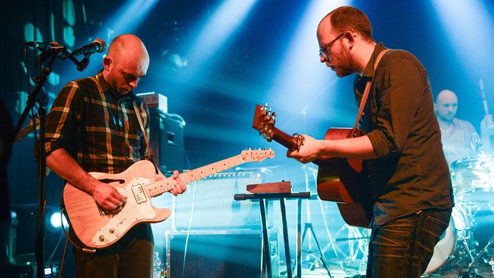 Sänger und Gitarrist der Band Honig stehen sich gegenüber und spielen sich heiße Töne zu