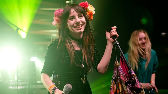 Iris strahlt nach Beendigung eines Songs. Am Ständer des Mikrofons hat sie bunte Tücher befestigt.