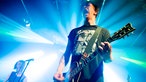 Gitarrist von John Coffey steht im Lichtkegel, hat den Mund weit auf und spielt seine E-Gitarre