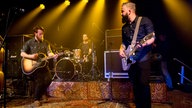 Die Gitarristen der Band Tim Vantol stehen nebeneinander auf der Bühne, der Schlagzeuger im Hintergrund, Lage wirkt entspannt
