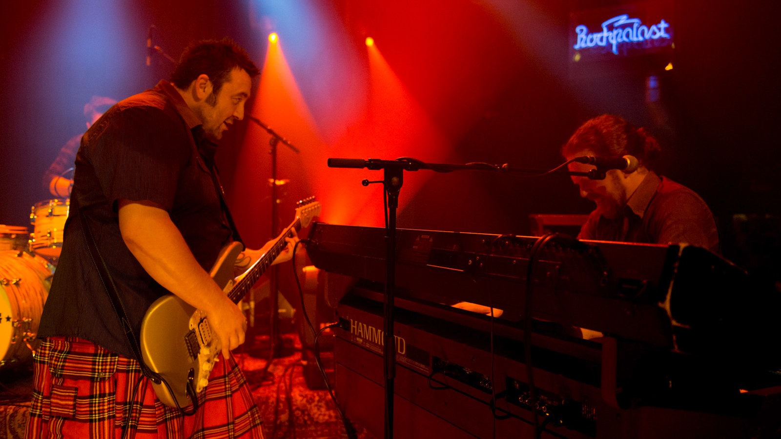 Gitarrist und Keyboarder von der Band King King stehen sich auf der Bühne gegenüber und schauen sich stimmungsvoll an, ihre Instrumente zwischen Ihnen. Die Rote Bühnenbeleuchtung untermalt die rockige Stimmung