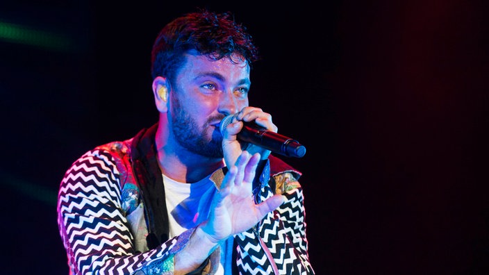 Marteria rappt, macht mit der Hand eine abwehrende Bewegung.