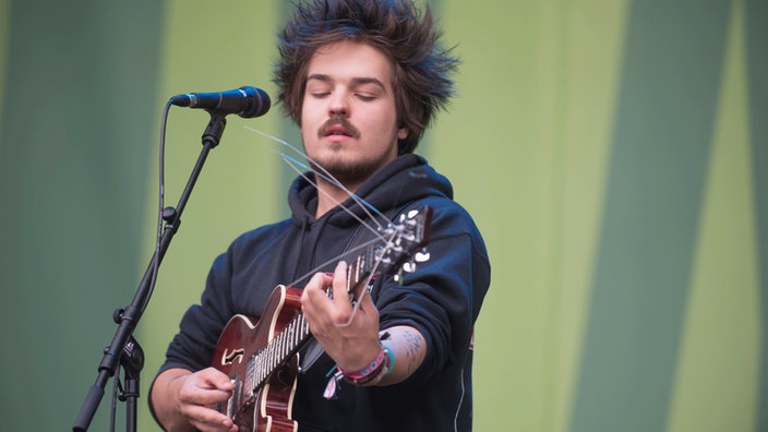 Clemens von Milky Chance, dessen Haarfrisur an Mecki den Igel erinnert, spielt konzentriert Gitarre. Den Blick hat er auf sein Instrument gesenkt.