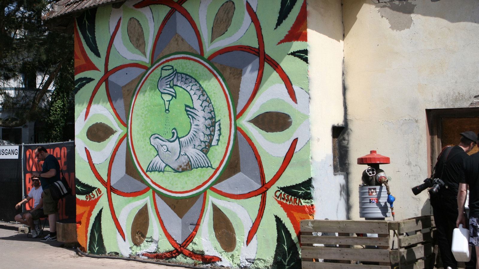 Auf einer Gebäudeaußenwand ist das Symbol des Orange Blossom Festivals aufgemalt, es ist ein schuppiger Fisch zu sehen der in seiner Schwanzflosse eine Flasch hält und dessen Inhalt in sein Maul kippt