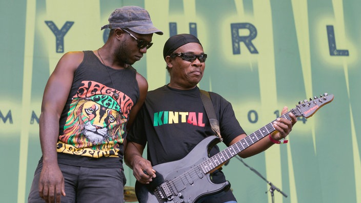 Keyboarder Demar Gayle hat sein Instrument verlassen, um Gitarrist Courtland White einen Support-Besuch abzustatten. Jetzt steht er neben ihn und schaut dem beim Spielen zu.
