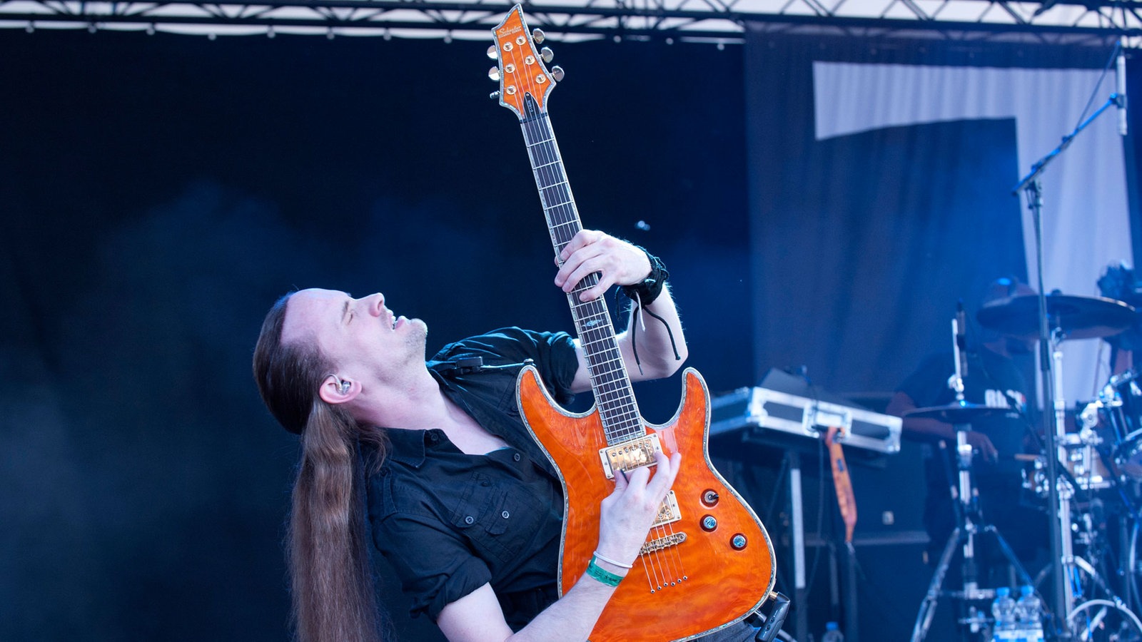 Der Gitarrist der Band lehnt sich nach hinten und streckt seine orangene Stratocaster-Gitarre in die Höhe
