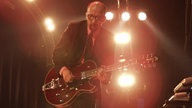 Garbage: Mann mit Glatze und Brille spielt Gitarre im Scheinwerferlicht