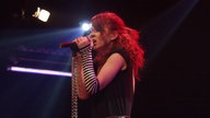 Garbage: Junge Frau mit roten Jahren und geringeltem Handschuh singt in ein Mikrofon