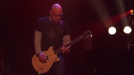 Garbage: Mann mit Glatze und Brille spielt im Halbdunkeln Gitarre auf der Bühne.