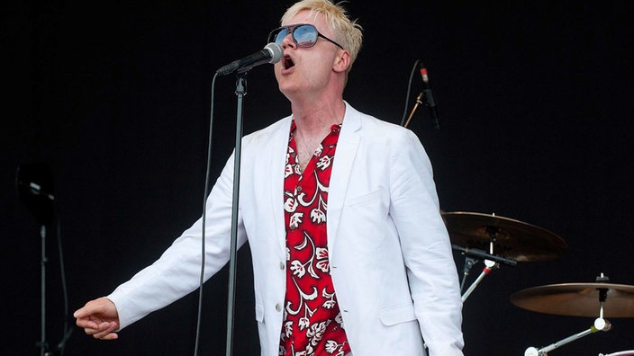 Sänger der Me First & The Gimme Gimmes singt ein lautes O ins Mikrofon, hat ein schönes weißes Jacket und ein Hawaii-Hemd an