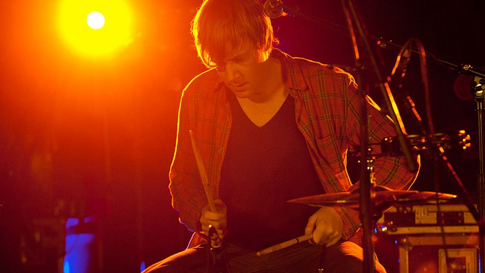 Der Drummer der Band An Horse wird von hinten orange angestrahlt.