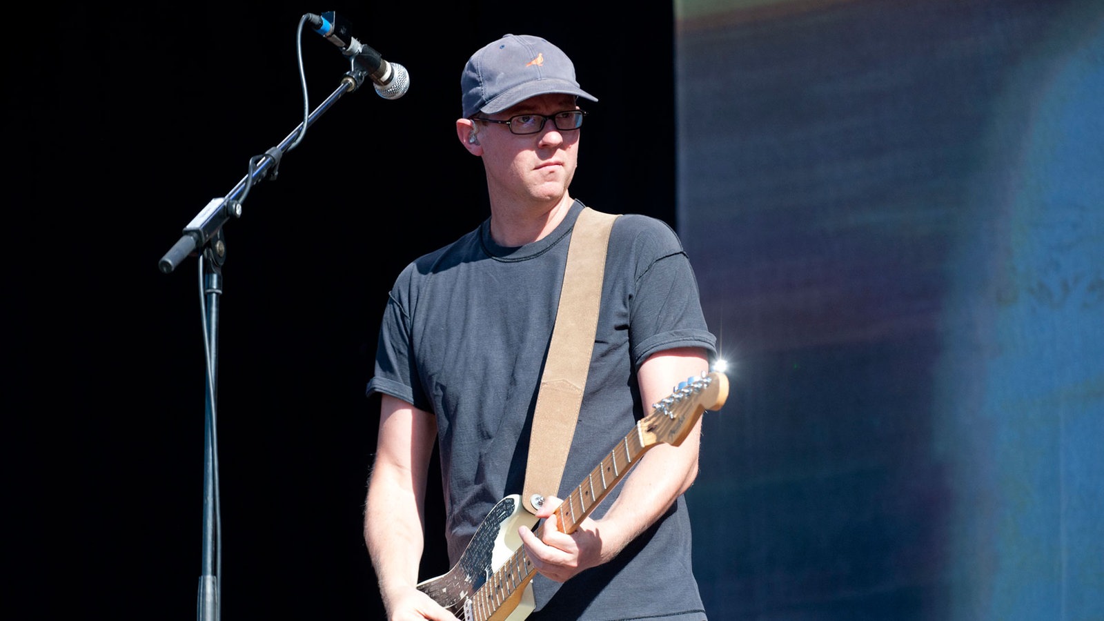 Mann mit Brille und Kappe spielt Gitarre und schaut zur Seite