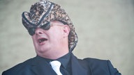 Dicker Mann mit Sonnenbrille und Leopardenfell-Cowboyhut.