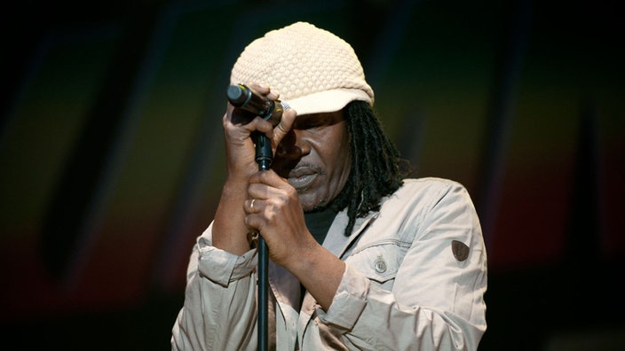 Ein Sänger mit Dread-Locks hält sich am Mikrofon-Ständer fest