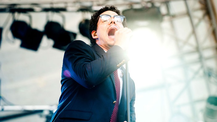 Ben L'Oncle Soul hält den Mikrofonständer uns singt mit weit aufgerissenem Mund