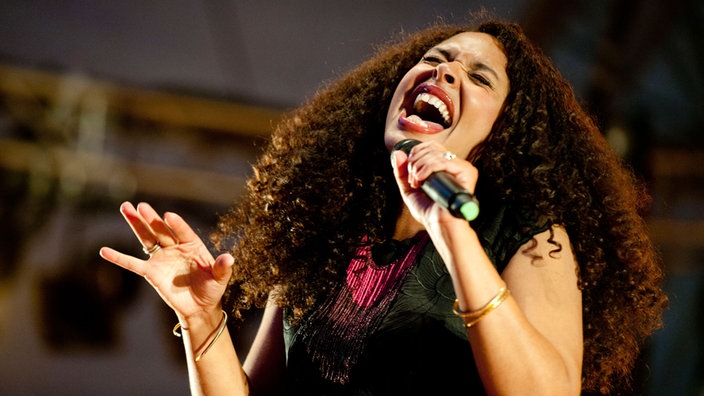Joy Denalane singt mit voller Hingabe in das Bühnenmikrofon. Sie hat sehr volle, rote Lippen