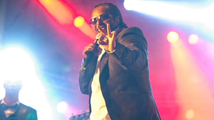 "Madcon"-Mitglied Yosef Wolde-Mariam formt einen Hasen mit der linken Hand. Er lächelt in die Kamera und trägt eine Sonnenbrille