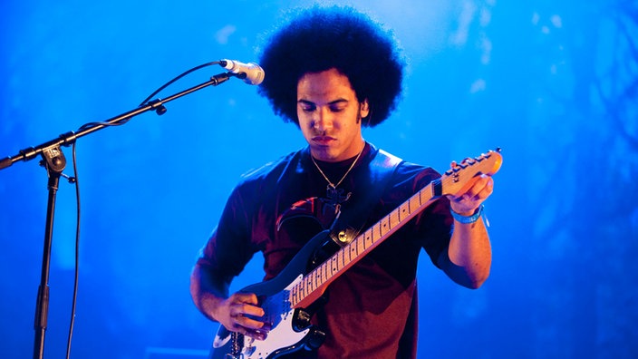 Patrice stimmt die Saiten siener Gitarre um ihn blaues Scheinwerferlicht