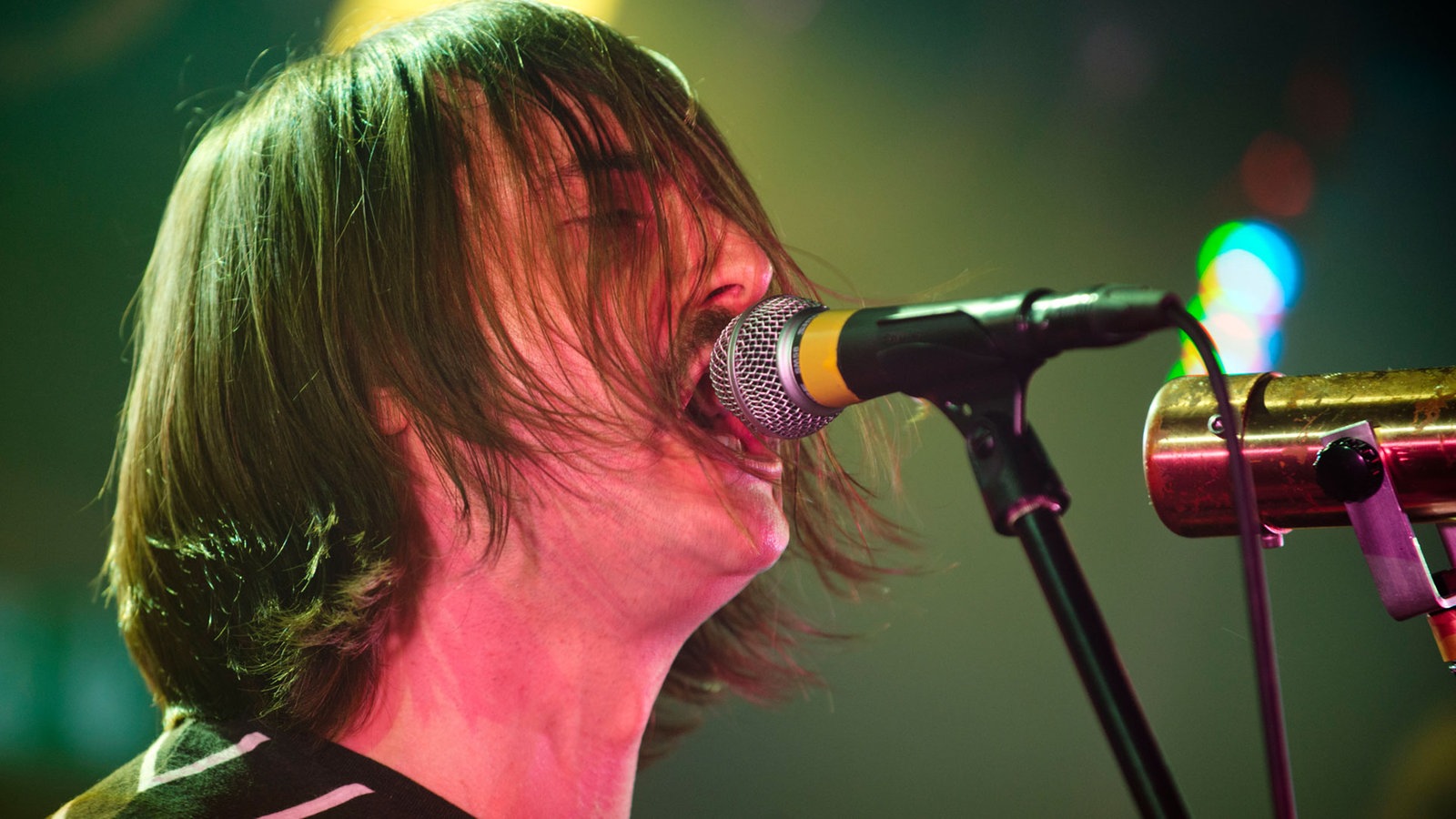 Der Sänger von "The Datsuns" singt in ein Mikrofon, im sind die Haare ins Gesicht gefallen