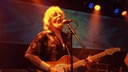 Mann mit grauen Haaren und Bart singt mit geschlossenen Augen und spielt Gitarre.