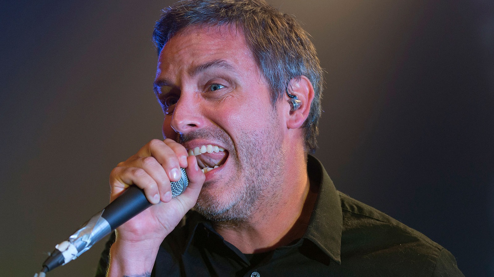 Portrait des Sängers, der mit angespannter Mine singt. Das Mikrofon hält er fest umfasst.