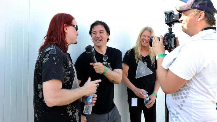 Rockpalast-Reporter Ingo Schmoll (Mitte) im Interview mit Mitgliedern der Band "Arch Enemy", ein Kameramann filmt sie