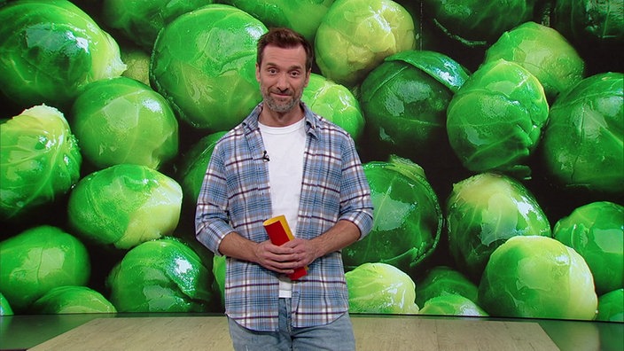  Daniel Aßman steht im Servicezeit-Studio. Im Hintergrund sieht man eine Nahaufnahme eines Dutzen Rosenkohls.
