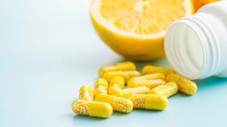 Gelbe Vitamin-C Präparate neben einer seitlich liegenden Aufbewahrungsdose, dahinter eine Zitronenhälfte.