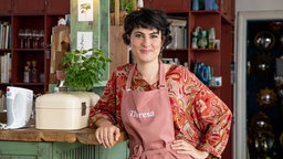 Das Bild zeigt eine dunkelhaarige Frau, die eine hellrote Schürze trägt 