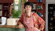 Das Bild zeigt eine dunkelhaarige Frau, die eine hellrote Schürze trägt 